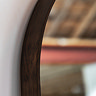close up image on rounded walnut edge of floor mirror, focus on dark brown wood and smooth glass