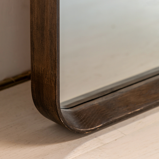 close up on walnut floor edge of mirror, focus on smooth glass and dark oak frame where it touches light wood floor