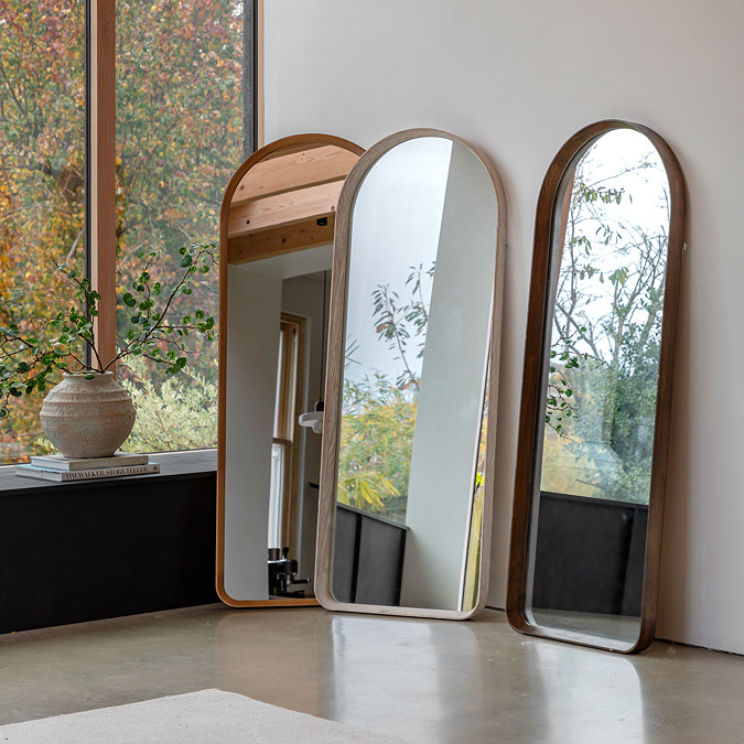 image of three wooden mirrors in varying oak shades leaning against a cream wall next to large window with foliage