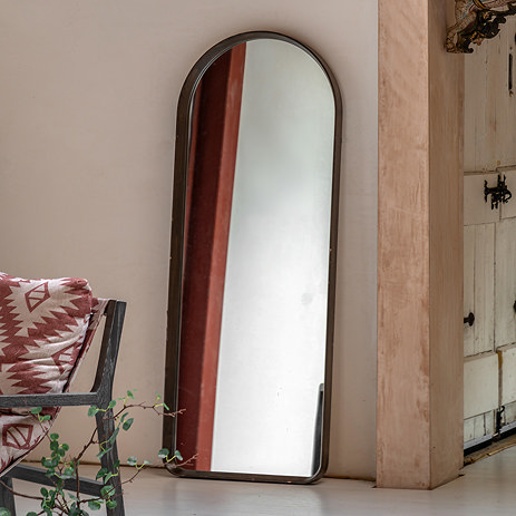 image of rounded walnut rectangular floor mirror leaning against beige wall