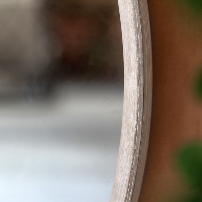 close up on middle section of rounded wall mirror, focus on lime wash of frame and smooth glass