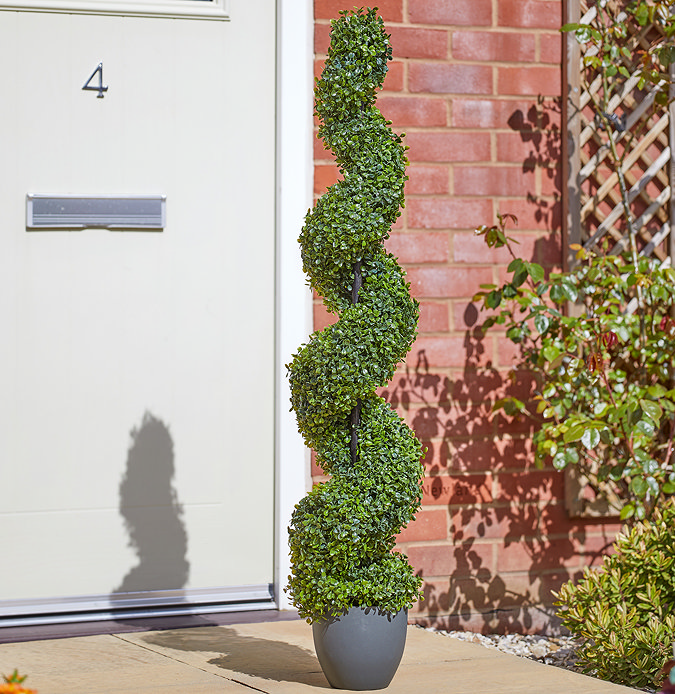 image of tall topiary twirl tree in grey pot, on open porch of a red brick house