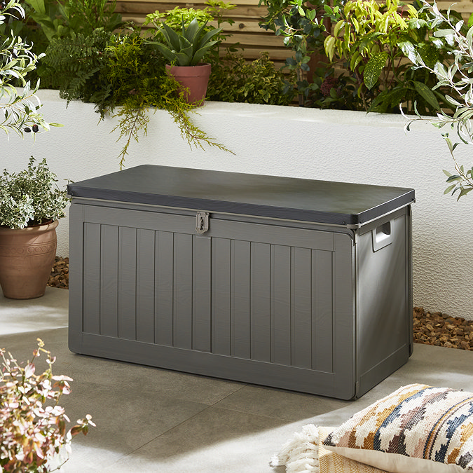 image of grey storage box with black lid, against a cream wall in garden