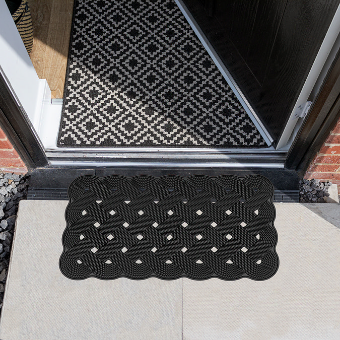 image of black rubber scraper mat with diamond pattern and wavy edges in front of house's open door
