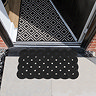 image of black rubber scraper mat with diamond pattern and wavy edges in front of house's open door