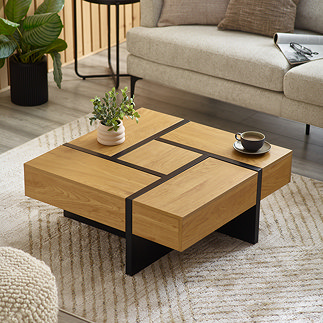 image of cubed light oak coffee table with black metal lines to separate concealed drawers that function as each corner of the table. on a cream woven rug next to a cream sofa