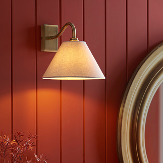 image of triangular wall light shade with curved antique brass arm, against a brick coloured panelled wall