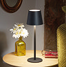 image of black sleek modern table lamp on light wood side table next to olive green sofa, emitting warm light