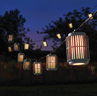 image of industrial style string lights strung up in a garden at night, emitting warm glow