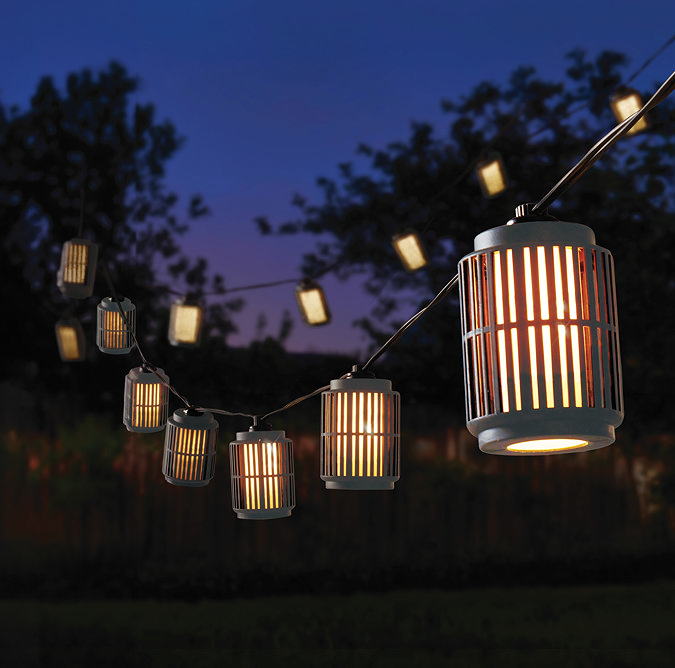 image of industrial style string lights strung up in a garden at night, emitting warm glow