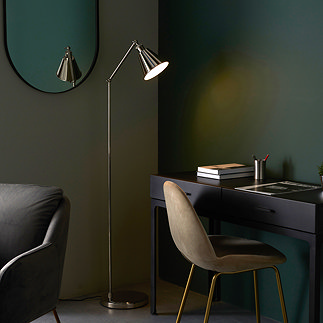 image of bright nickel floor lamp with conical shade in a dark green room shining light over modern black desk
