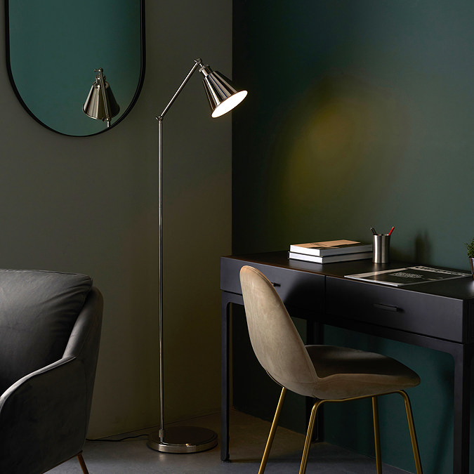 image of bright nickel floor lamp with conical shade in a dark green room shining light over modern black desk