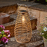 image of tall rattan lantern with handle, on stone garden step emitting warm white light at dusk