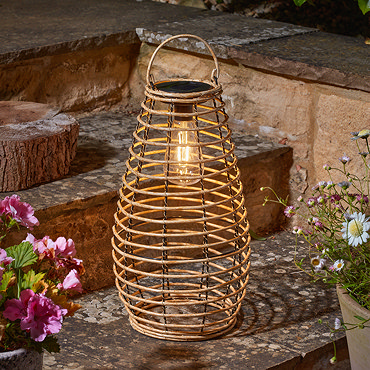 image taken during the day of tall rattan garden lantern on a wooden table