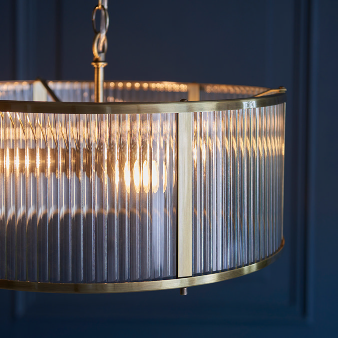 close up image of ribbed glass pendant light with antique brass metalwork edges and bulb within emitting warm glow