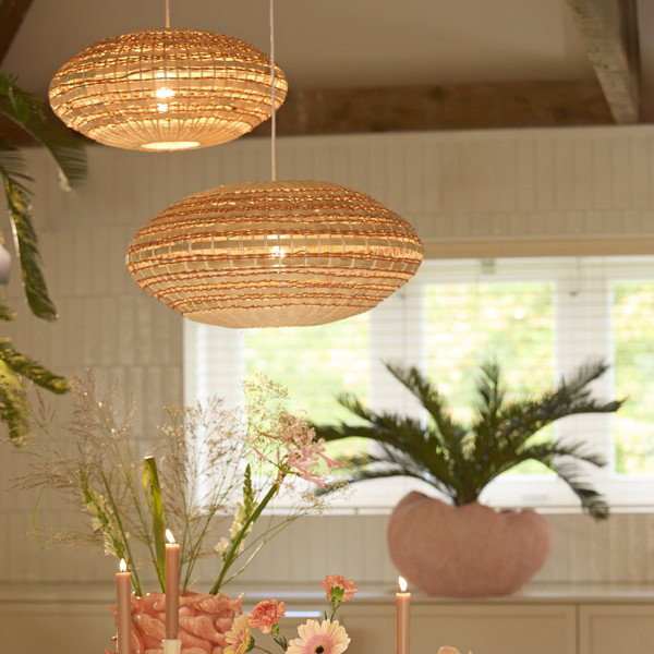 image of two oval hanging rattan light shades, small and large, in natural and terracotta colours hanging over dining table and emitting warm glow