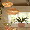image of two oval hanging rattan light shades, small and large, in natural and terracotta colours hanging over dining table and emitting warm glow