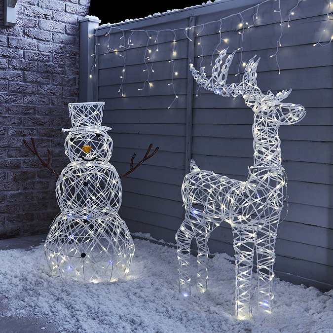 white rattan light up reindeer stood next to white rattan light up snowman at the front of a house sprinkled with light snow.