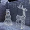 white rattan light up reindeer stood next to white rattan light up snowman at the front of a house sprinkled with light snow.