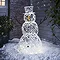 white rattan light up snowman in front of house on a snowy driveway, lit up at night.