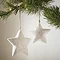 small rustic star and its larger counterpart hanging next to each other on a christmas tree, with cream wall in the background.