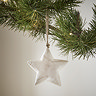 close up on small white wood rustic star, hanging from a christmas tree.
