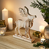 angled image of a rustic whitewashed wooden stag decoration stood on a sideboard, surrounded by candles and a potted plant.