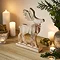 angled image of a rustic whitewashed wooden stag decoration stood on a sideboard, surrounded by candles and a potted plant.