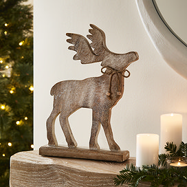 large wooden whitewashed stag decoration stood atop a mantlepiece next to some candles and a garland.