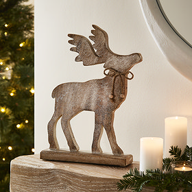 large wooden whitewashed stag decoration stood atop a mantlepiece next to some candles and a garland.