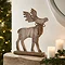 large wooden whitewashed stag decoration stood atop a mantlepiece next to some candles and a garland.