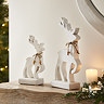 small white wooden standing reindeer next to larger white wooden reindeer on a mantlepiece, framed by cosy candles