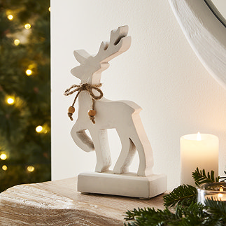 small white standing reindeer on the mantlepiece, framed by cosy lit candles and a christmas tree in the background