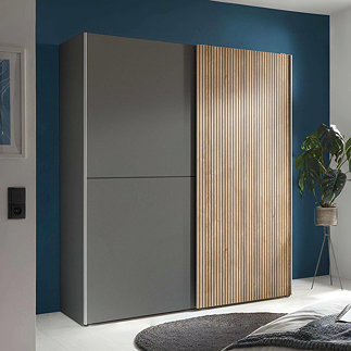 image of wide wardrobe with two sliding doors, one grey and one thin wood-panel effect, against teal wall in a bedroom