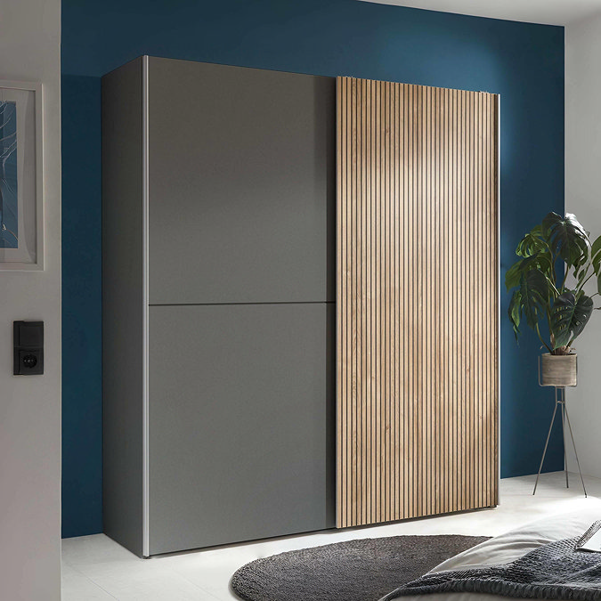 image of wide wardrobe with two sliding doors, one grey and one thin wood-panel effect, against teal wall in a bedroom