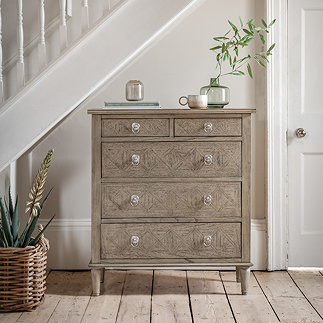 image of 5 drawer chest next to stairs in hallway, with potted plant on top