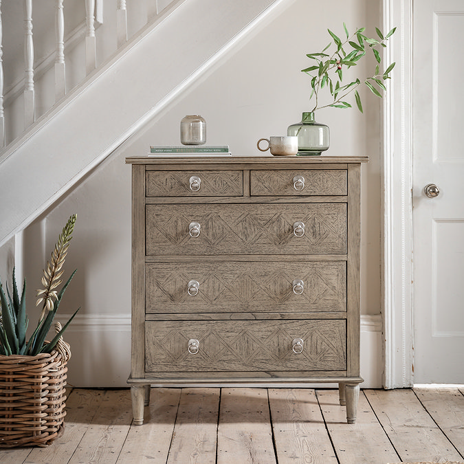 image of 5 drawer chest next to stairs in hallway, with potted plant on top