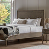 image of solid ashy wood bed with subtle pattern, against a panelled wall, dressed with duvet and monochrome throw