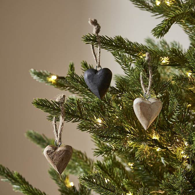 small wooden heart decorations hanging on branches of a lit christmas tree
