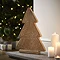 angled mage of wooden patterned tree decoration stood on a hearth next to a trio of pillar candles, with christmas tree blurred in the background. 