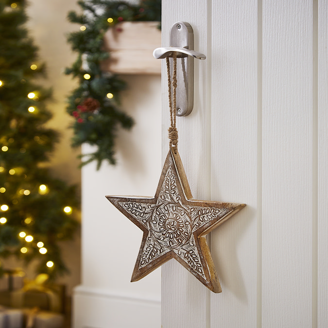 wooden patterned star hanging on a door handle with christmas tree in the background