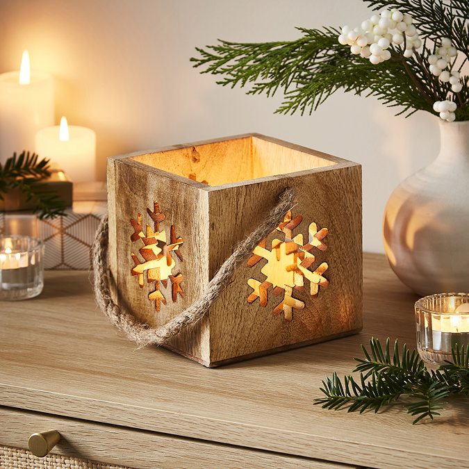 wooden cube tealight candle holder placed on a sideboard surrounded by warm candles and potted plant.