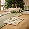 set of four placemats with festive woodland trees dotted on them, placed on a warm wood dining table with sage green table runner