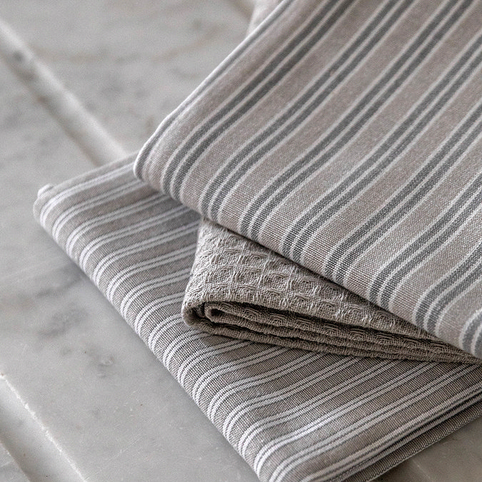 close up image of grey stripe tea towels folded up on top of each other on a marble counter, highlighting slight pattern variation of the set