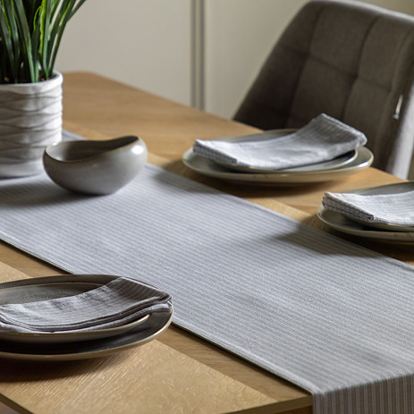 image of grey stripe table runner on a light oak table, plates on top with matching stripe napkins folded in them