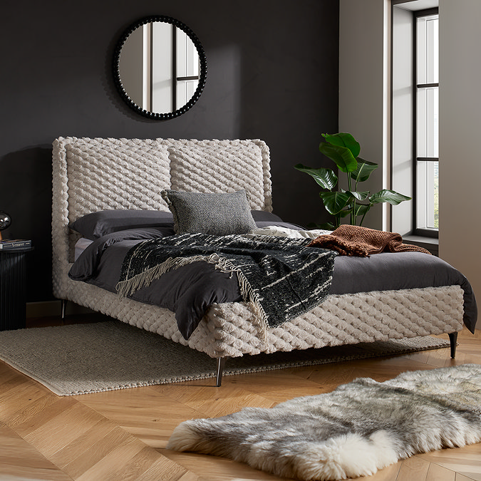 image of bed with faux fur bobbled headboard in white, dressed with grey duvet cover, against a dark grey wall with mirror above