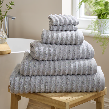image of set of silver-grey ribbed towels stacked on top of one another on a wooden side table next to a bath
