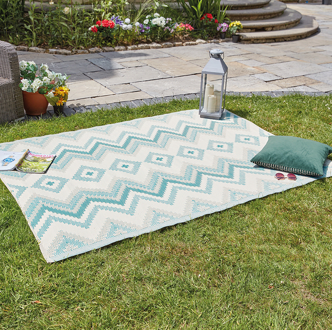 image of green zigzag rug on grass with lantern, cushion, and book on its edge